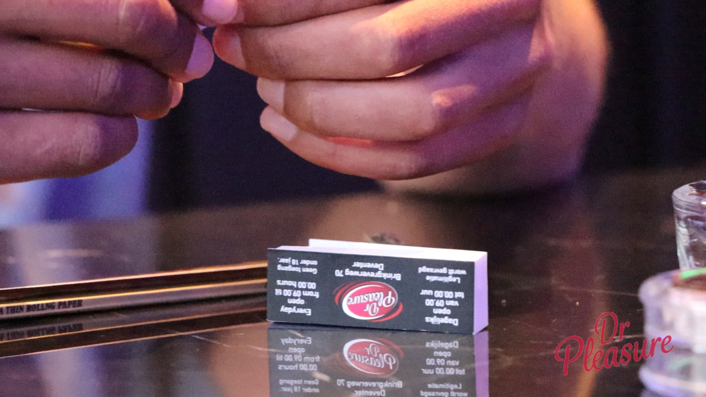 Een klant rolt een joint aan een tafel in coffeeshop Dr Pleasure