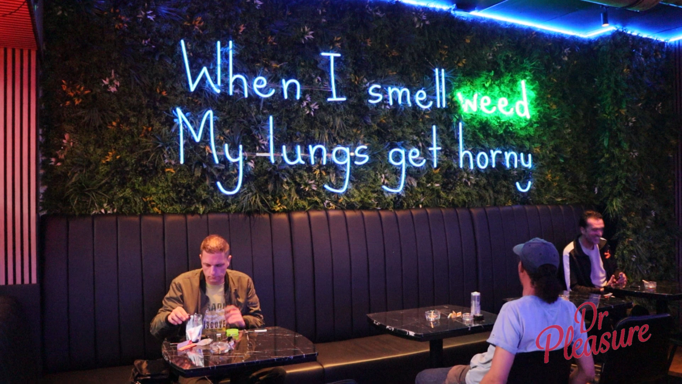 Gasten ontspannen onder de iconische neon-tekst "When I smell weed My lungs get horny"