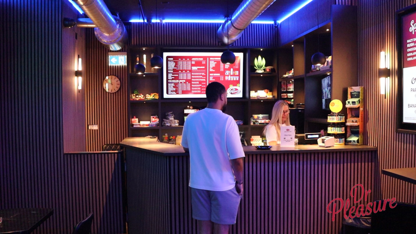 Een bezoeker bekijkt het menu en bestelt aan de balie van coffeeshop Dr Pleasure